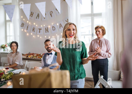 Happy surprised young woman receiving a gift on indoor party. Stock Photo