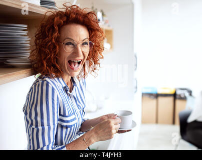 A portrait of joyful businesswoman in an office, holding a cup of coffee and laughing. Stock Photo