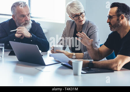Corporate business team sitting at a table with laptop discussing new project.  Mature man discussing new business ideas with colleagues at office. Stock Photo