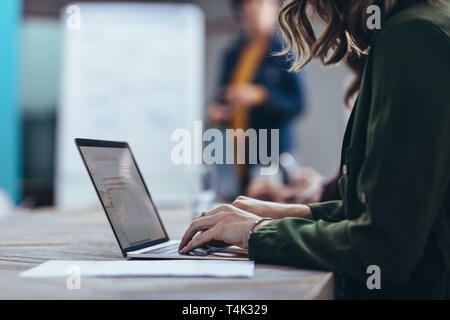 Cropped shot of woman working on laptop while sitting in meeting in conference room. Female executive using laptop during a presentation in office. Stock Photo