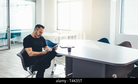 Mid adult businessman working on his digital tablet in a bright office. Entrepreneur with his tablet computer in a modern office space. Stock Photo
