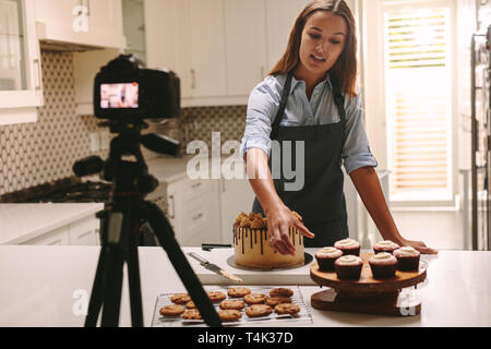 Social media influencer woman recording video content in kitchen, showing confectionery on table. Female confectioner filming herself of her online cu Stock Photo