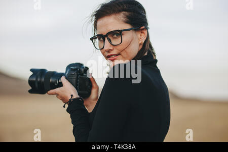 Young female photographer photo shooting outdoors. Caucasian woman in casual holding a dslr camera. Stock Photo