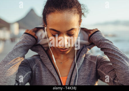 Close up of fitness woman wearing a hooded shirt and earphones outdoors. Female runner on outdoors workout. Stock Photo