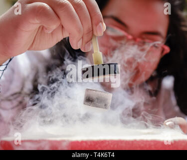 Female Student Demonstrates Quantum Magnetic Levitation and Suspension Effect. A splash of liquid nitrogen cools a ceramic superconductor forcing it t Stock Photo