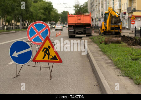 Road signs, detour, road repair on street background, truck and excavator digging hole Stock Photo