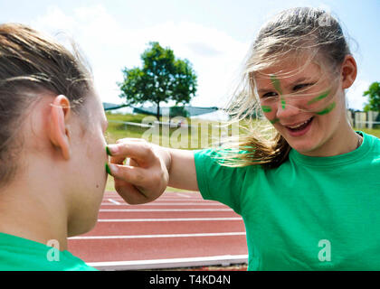 Girl putting green face paint on friend for house athletics day, UK. Stock Photo