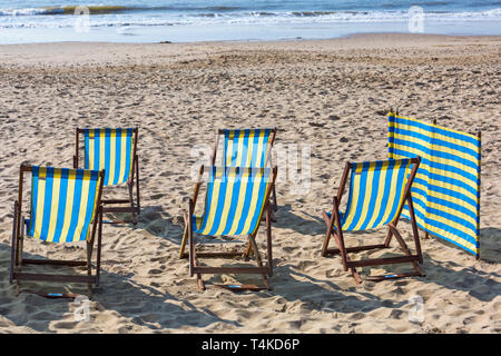 Five empty deckchairs and windbreak for hire on beach at Bournemouth, Dorset UK in April Stock Photo