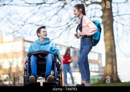 Teenage Boy In Wheelchair Talking With Female Friend As They Leave High School Stock Photo