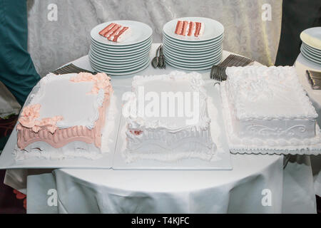 Dessert table in restaurant with three white wedding cakes decorated with whipped cream. Stock Photo