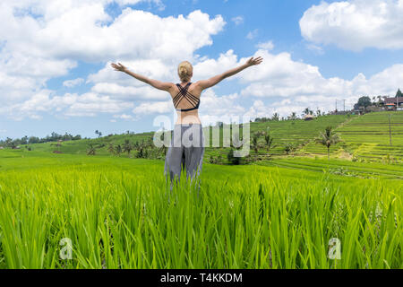 Relaxed healthy sporty woman, arms rised to the sky, enjoying pure nature at beautiful green rice fields on Bali. Stock Photo