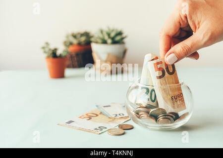 Accumulation of money in a glass jar, female hand puts euro banknotes in a glass piggy bank Stock Photo