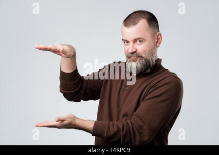 Smiling mature caucasian man showing big size with both hands. Confident european male with beard demonstrating large space or holding object, copy sp Stock Photo
