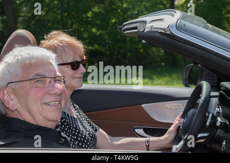 Happy older couple drives with a luxury convertible car Stock Photo