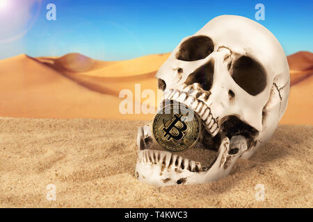 Close up on skull biting bitcoin over sand background. Concept of investment and fluctuation danger of bitcoin and cryptocurrency. Stock Photo