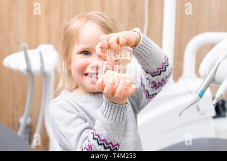 Little child sitting in a dental chair showing artificial model of child's jaw in pediatric dental clinic, focus on jaw Stock Photo