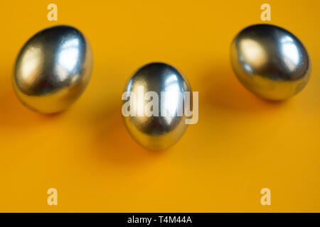 three silver eggs lie on a bright yellow background Stock Photo