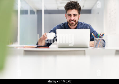 Young programmer is working on laptop. Computer in the office while having coffee Stock Photo