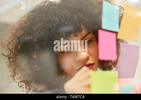 Young African businesswoman is writing down ideas on colorful notes while brainstorming Stock Photo