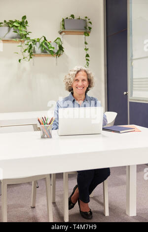 Smiling senior woman is working on laptop computer at coworking workplace Stock Photo