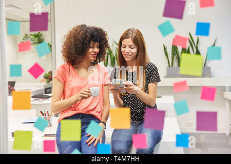 Two young business women together read a text message on a smartphone in the office Stock Photo