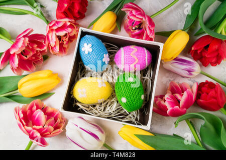 Easter background with colorful knitted Easter eggs and tulip flowers on stone background.  Easter background, handmade holidays decorations and gift  Stock Photo