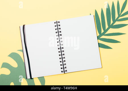 Summer flat lay composition open blank white notebook on paper green tropical leaves over yellow background, view from above. Stock Photo