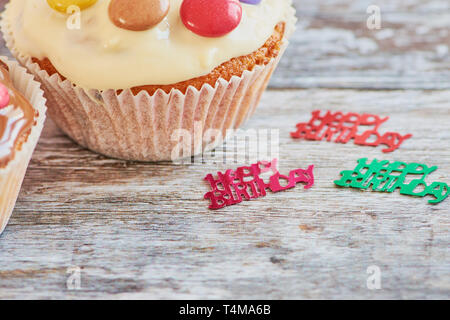 muffin coated with chocolate and chocolate lentils on a wooden surface with decoration showing the words happy birthday Stock Photo