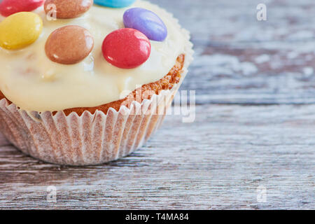 close up of one muffin coated with white chocolate and chocolate lentils on it againt wooden background with copy space Stock Photo