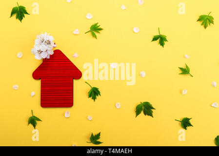 Red toy House, white flowers on a yellow background with green leaves. Real estate business concept, Space for text, Affordable housing for families Stock Photo