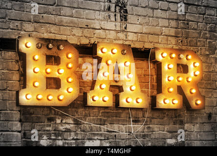 Bar signboard. Inscription from large metal letters decorated with glowing light bulbs on the brick wall Stock Photo