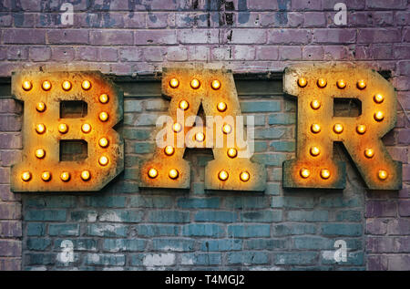 Bar signboard. Inscription from large metal letters decorated with glowing light bulbs on the brick wall Stock Photo