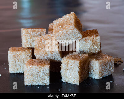 Heap of brown sugar cubes on a black surface. Stock Photo