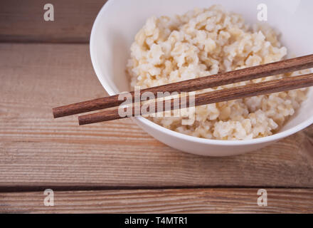 Cooked brown rice in white bowl with chopsticks on the old wooden table Stock Photo