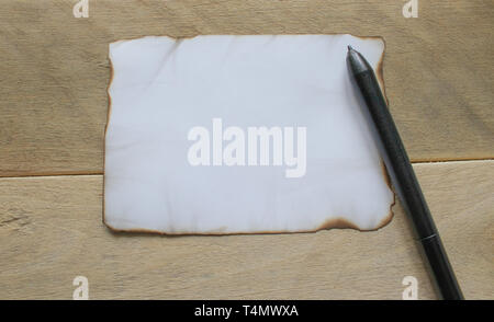On wooden boards, there is a black pen, a white sheet of paper burnt at the edges, leaving room for text. Concept background. Stock Photo
