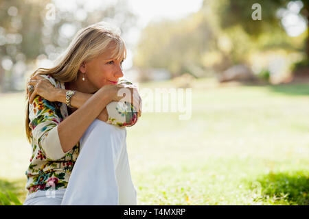 Mature woman sitting in a park looking thoughtful. Stock Photo