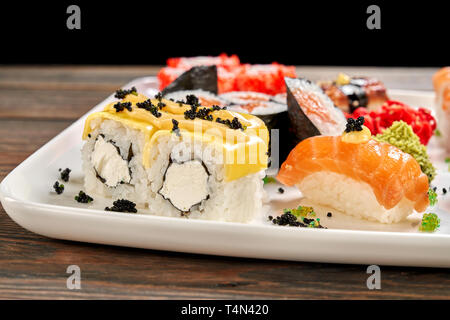 Delicious cheese rolls with cream cheese, decorated with black caviar and mayo. Set of sushi, sake nigiri, sake maki, wasabi and pickled ginger. Stock Photo