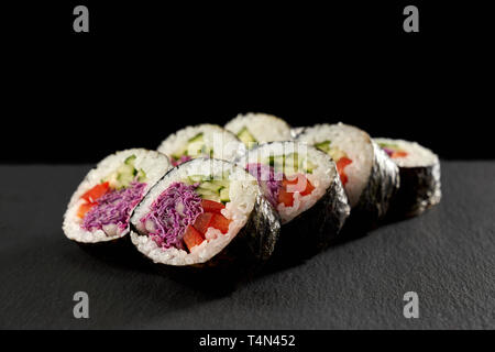 Vegetarian maki filled with cucumber or kappa, red paprika and violet cabbage. Veggie rolls wrapped in nori, served on black stone. Stock Photo