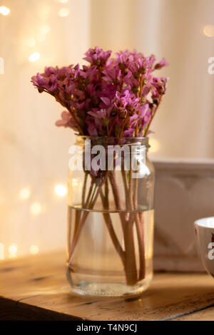 Pink Bergenia flowers in a clear glass vase on a wooden surface with a blurred bokeh background - flowers floral pink feminine Stock Photo