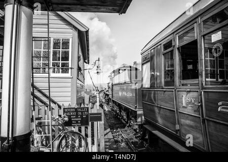 Black & white morning scene on vintage steam railway line, UK. Vintage steam train departure, Bewdley station; signalman in signal box watching train. Stock Photo