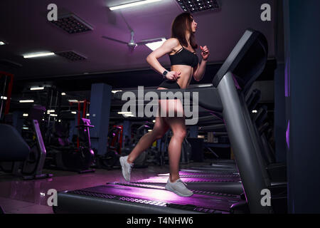 Active young woman and man running on treadmill in gym.
