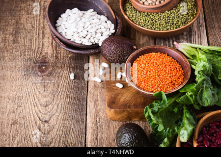 Variety of beans and legumes, fresh vegetables, healthy plant based vegan food, close up, selective focus. Cooking ingredients on rustic wooden table Stock Photo