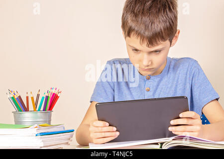 Kid sitting at table with books notebooks and using tablet computer Stock Photo
