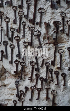 A bunch of old black metal keys on display on a white wall hanging from nails Stock Photo