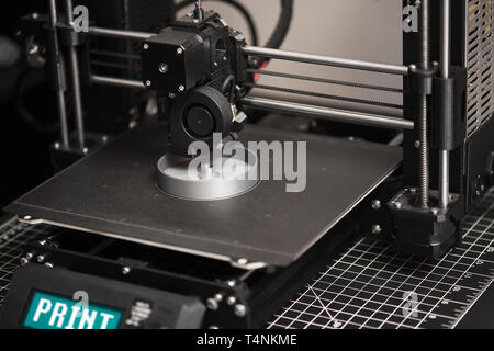 A 3D printer in the process of printing a digital file or part with gray colored filament on the metal heatbed. Stock Photo