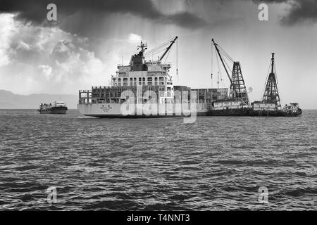 Moody Black and White Photo Of The WAN HAI LINES Container Ship, WAN HAI 303, Unloading Shipping Containers In A Mid-Stream Operation, Hong Kong. Stock Photo