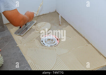 Spreading wet mortar before applying tiles on bathroom floor tile. Stock Photo