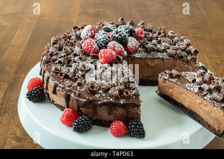 A decadent Chocolate Mousse Cake with chocolate ganache and topped with Raspberries, Blackberries and chocolate curls on a wood table Stock Photo