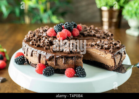 A decadent Chocolate Mousse Cake with chocolate ganache and topped with Raspberries, Blackberries and chocolate curls on a wood table Stock Photo