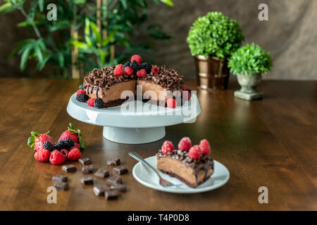 A decadent Chocolate Mousse Cake with chocolate ganache and topped with Raspberries, Blackberries and chocolate curls on a wood table Stock Photo